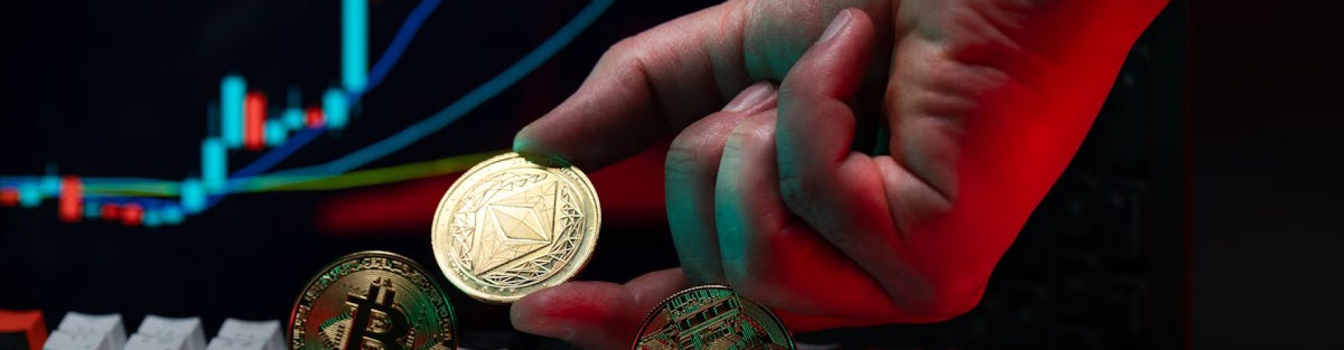 Close-up of a hand holding cryptocurrency coins on keyboard, with a graph display in the background.